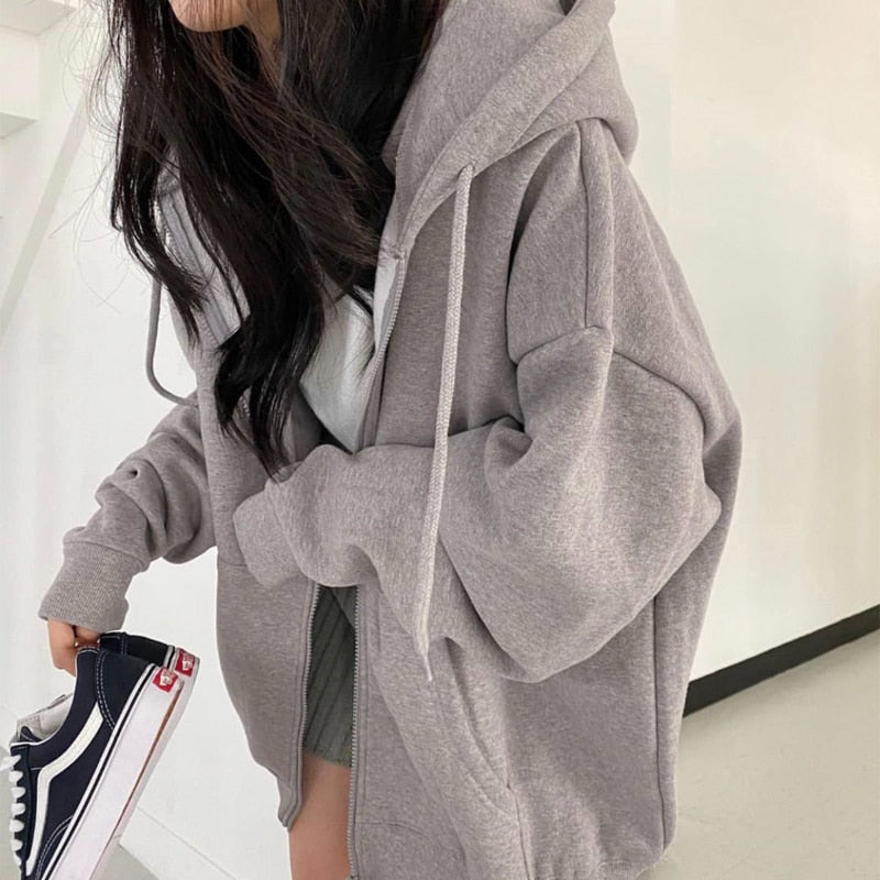 Frau in grauem Kapuzenpullover, hält schwarze Sneaker, lässige Mode, Streetwear-Look.