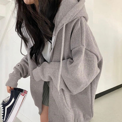 Frau in grauem Oversize-Hoodie, hält schwarze Sneaker, lässiger Streetwear-Look.