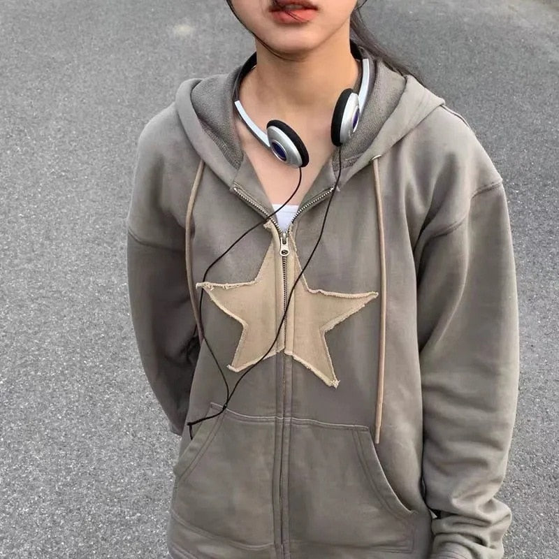 Grauer Kapuzenpullover mit Sternmotiv, Kopfhörer um den Hals, lässige Straßenmode.