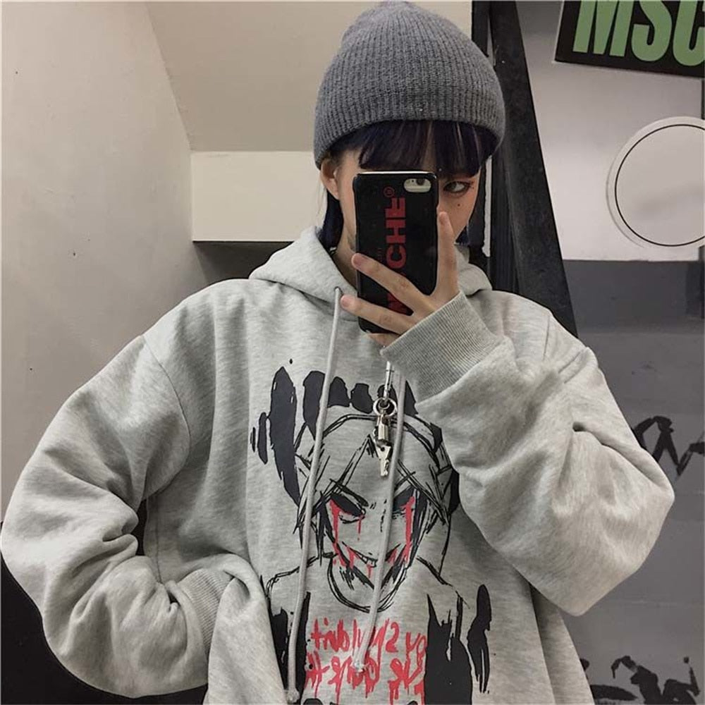 Person in grauem Hoodie mit grafischem Design, grauer Mütze, hält Smartphone, urbaner Stil.
