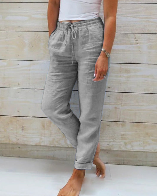 Frau trägt graue Leinenhose, lässig, mit Taschen, vor Holzwand, Sommermode.