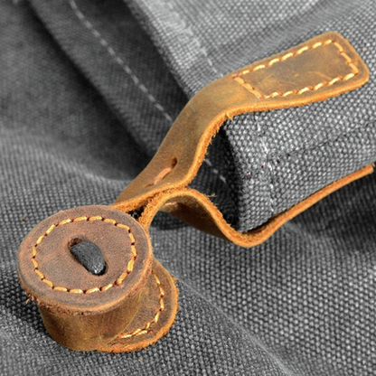 Graue Stofftasche mit braunem Lederknopf, robuste Nähte, modisches Accessoire.