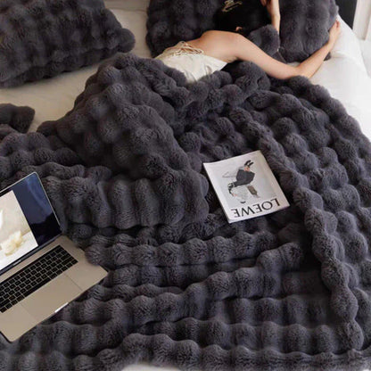 Graue, flauschige Decke auf Bett mit Laptop und Zeitschrift, gemütliches Schlafzimmer-Setup.