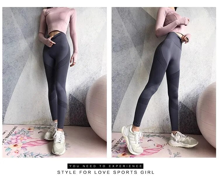 Frau in grauer Sportleggings und rosa Oberteil, posiert vor Wand, trägt weiße Turnschuhe.