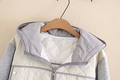 Graue Kapuzenjacke mit Reißverschluss, gesteppte Vorderseite, hängend auf Holzkleiderbügel.