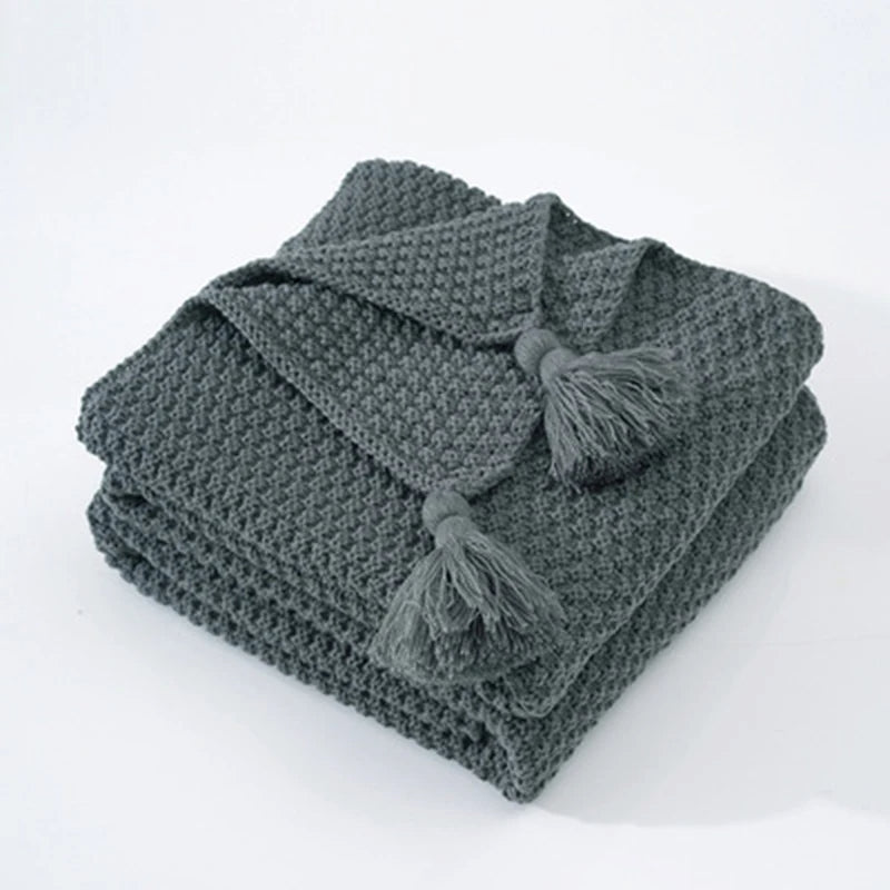 Graue Strickdecke mit Quasten, weiches Baumwollmaterial, ideal für Wohnzimmer oder Schlafzimmer.