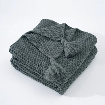 Graue Strickdecke mit Quasten, weiches Baumwollmaterial, ideal für Wohnzimmer oder Schlafzimmer.