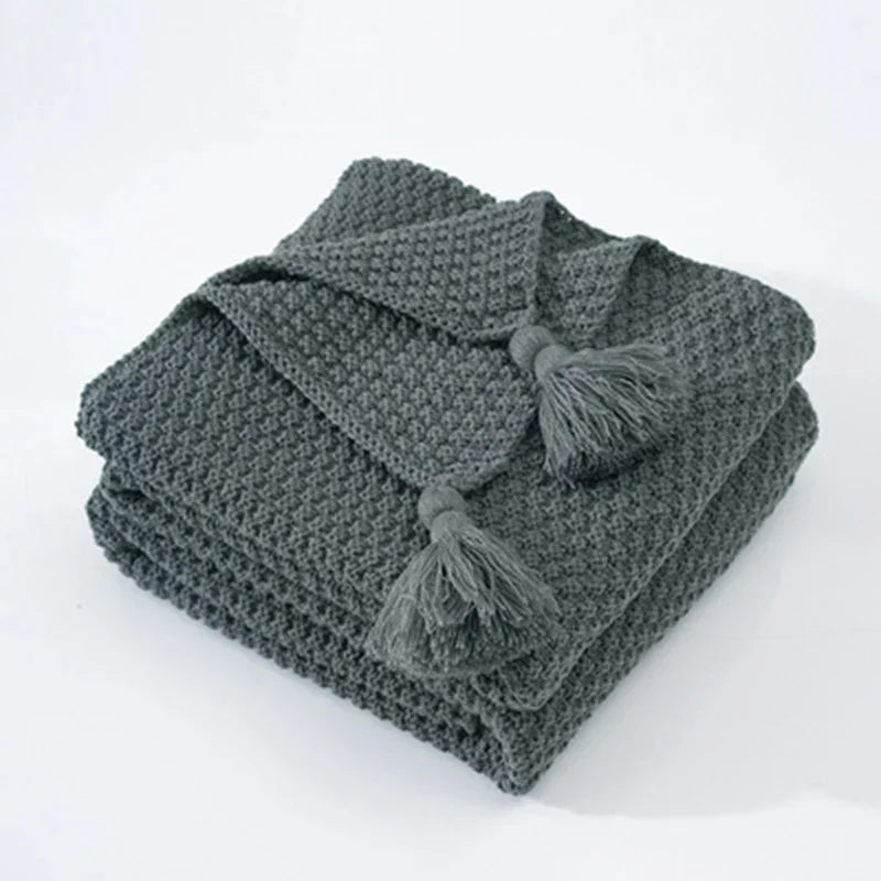 Graue Strickdecke mit Quasten, weiches Material, ideal für Wohnzimmer, gemütliche Wohnaccessoires.
