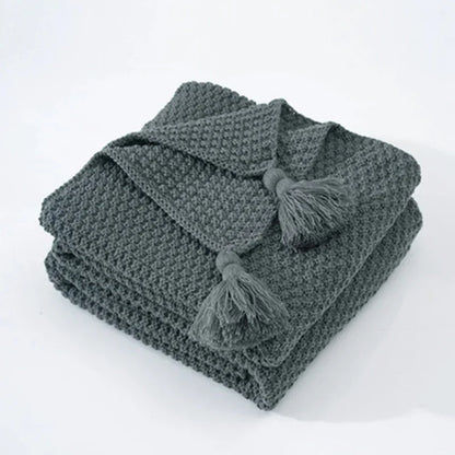 Graue Strickdecke mit Quasten, weiches Material, ideal für Wohnzimmer, gemütliche Wohnaccessoires.