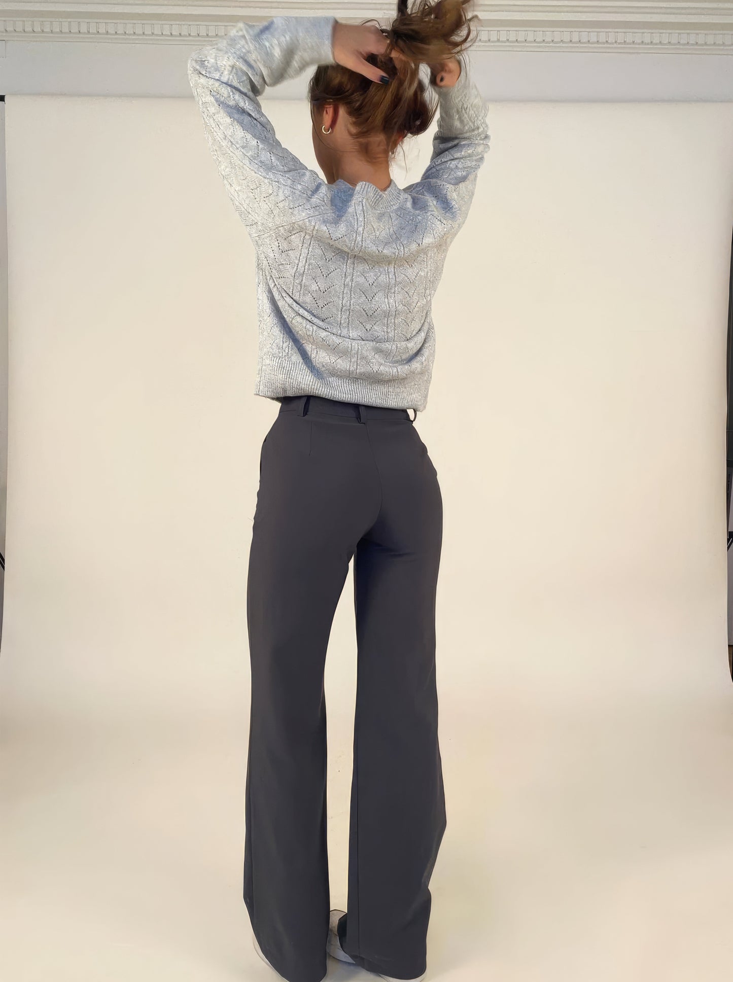 Frau in grauem Strickpullover und dunkelgrauer Hose, Rückansicht, modisch, elegant.