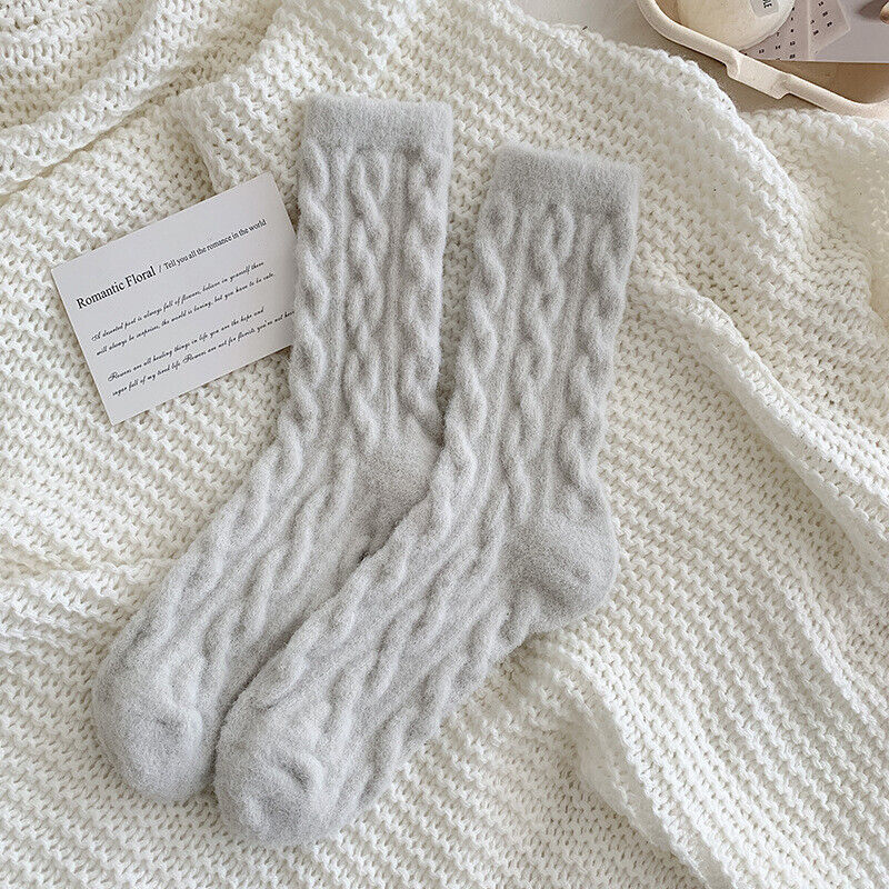 Graue Stricksocken aus Wolle auf weißem Strickhintergrund, gemütlich, warm, wintertauglich.