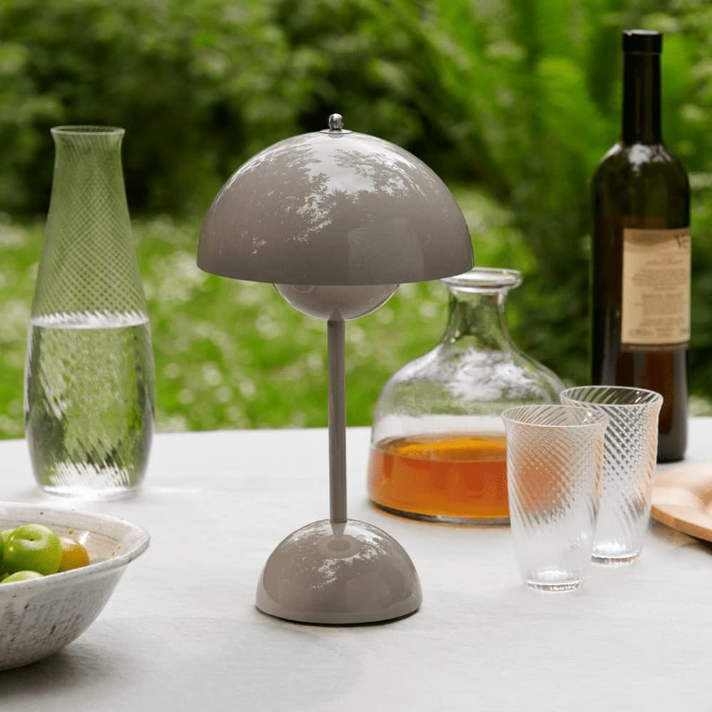 Graue Tischlampe aus Metall auf Gartentisch, umgeben von Karaffen und Gläsern im Freien.