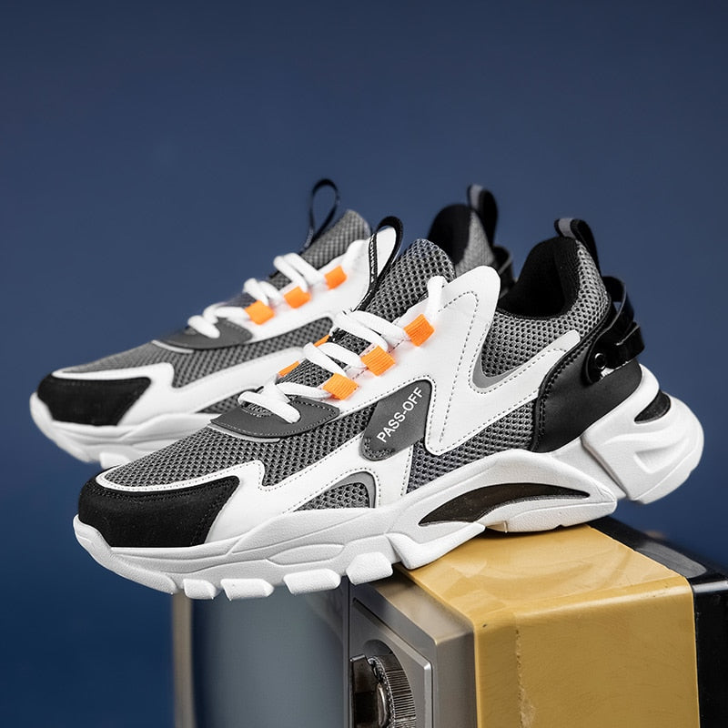 Graue und weiße Sneaker mit Mesh-Obermaterial und orangefarbenen Akzenten auf blauem Hintergrund.