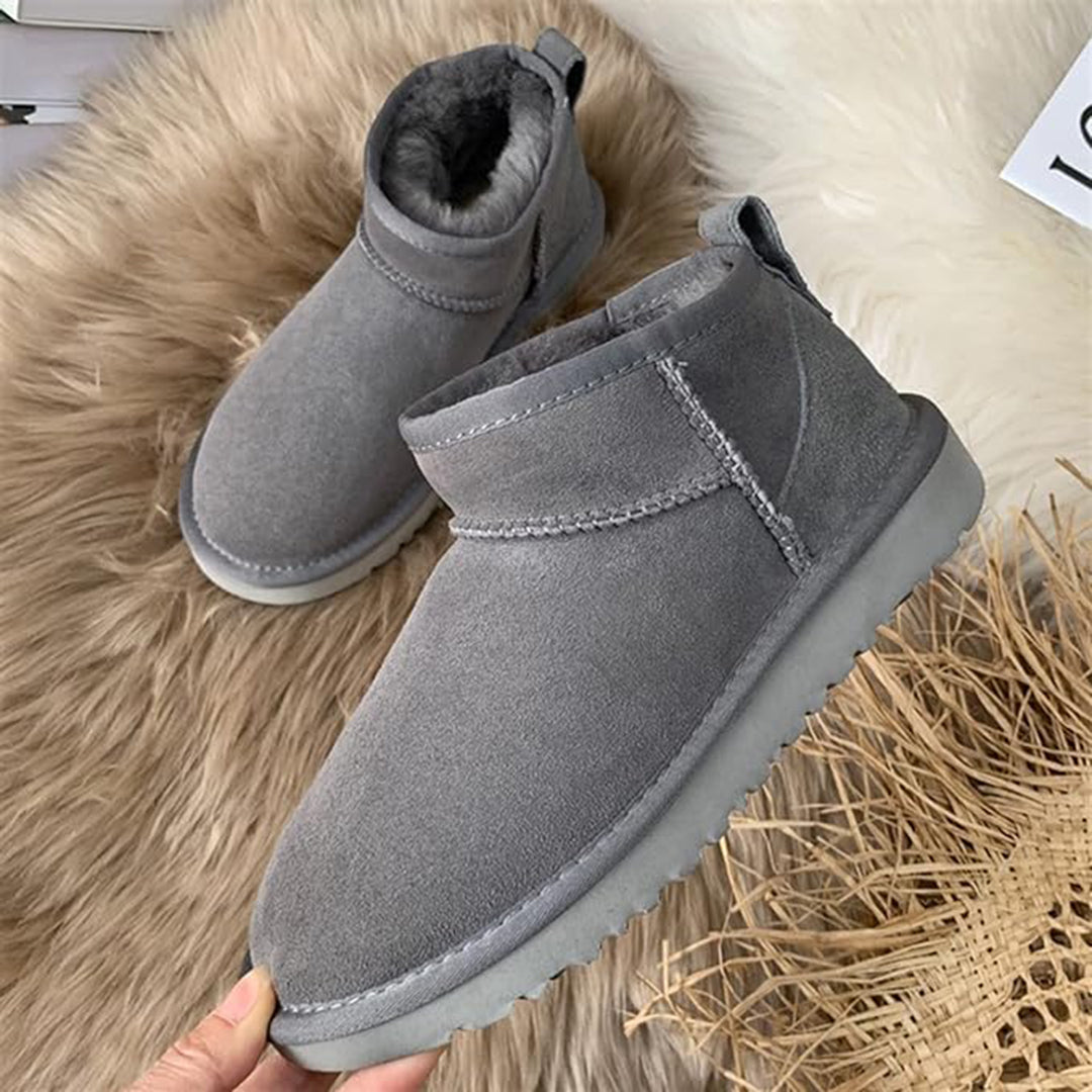 Graue Winterstiefel aus Wildleder mit Fellfutter auf Fellteppich.
