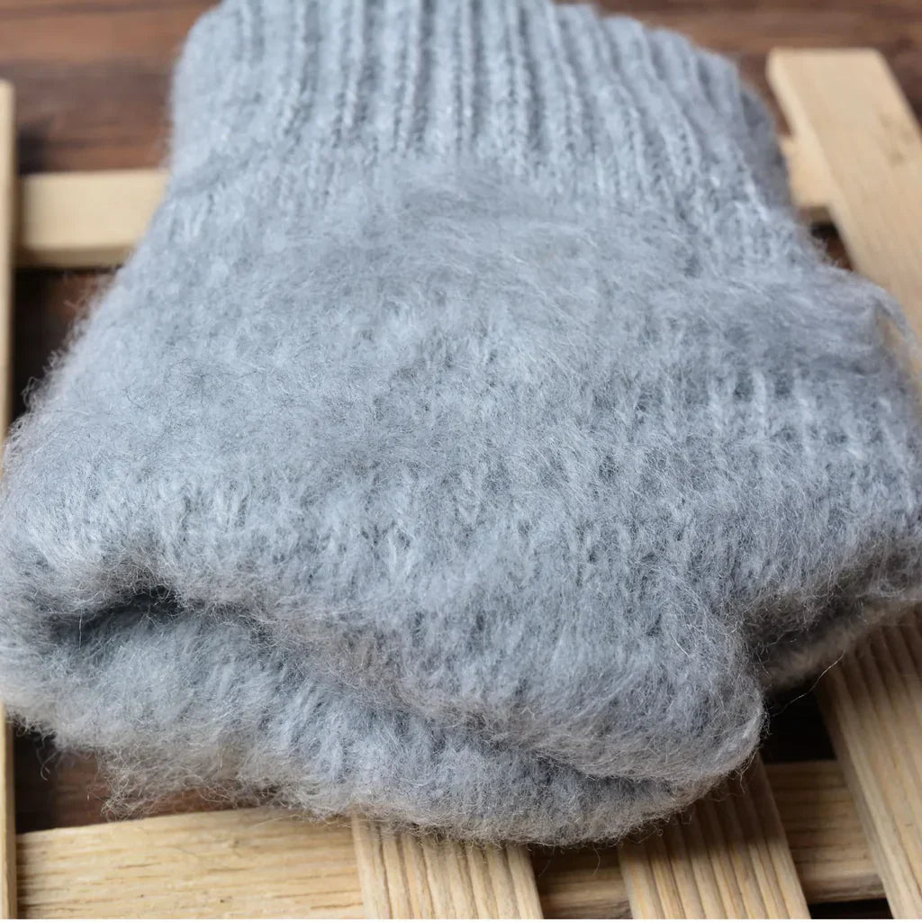 Graue Wollsocken aus Alpaka, handgestrickt, warm, weich, auf Holzuntergrund.
