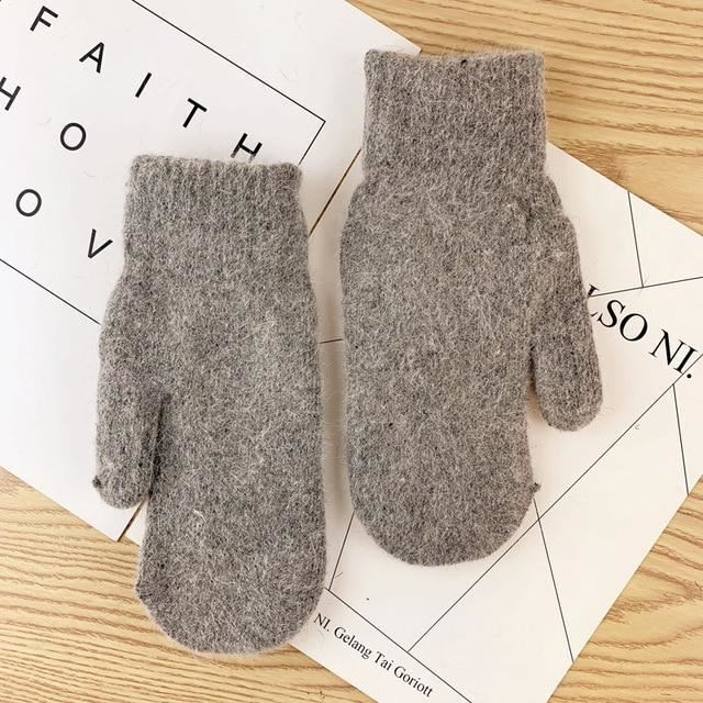 Graue Wollfäustlinge auf Holztisch, warme Winterhandschuhe, gestrickt, gemütlich.