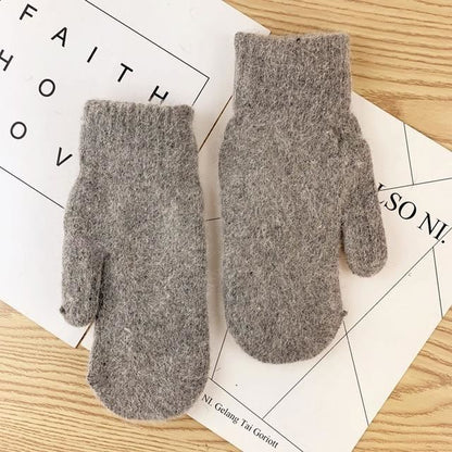 Graue Wollfäustlinge auf Holztisch, warme Winterhandschuhe, gestrickt, gemütlich.