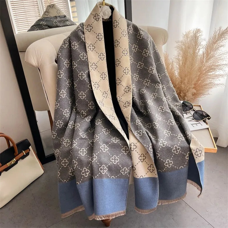 Grauer Wollschal mit Blumenmuster, blauem Rand, auf Stuhl drapiert, elegantes Design.