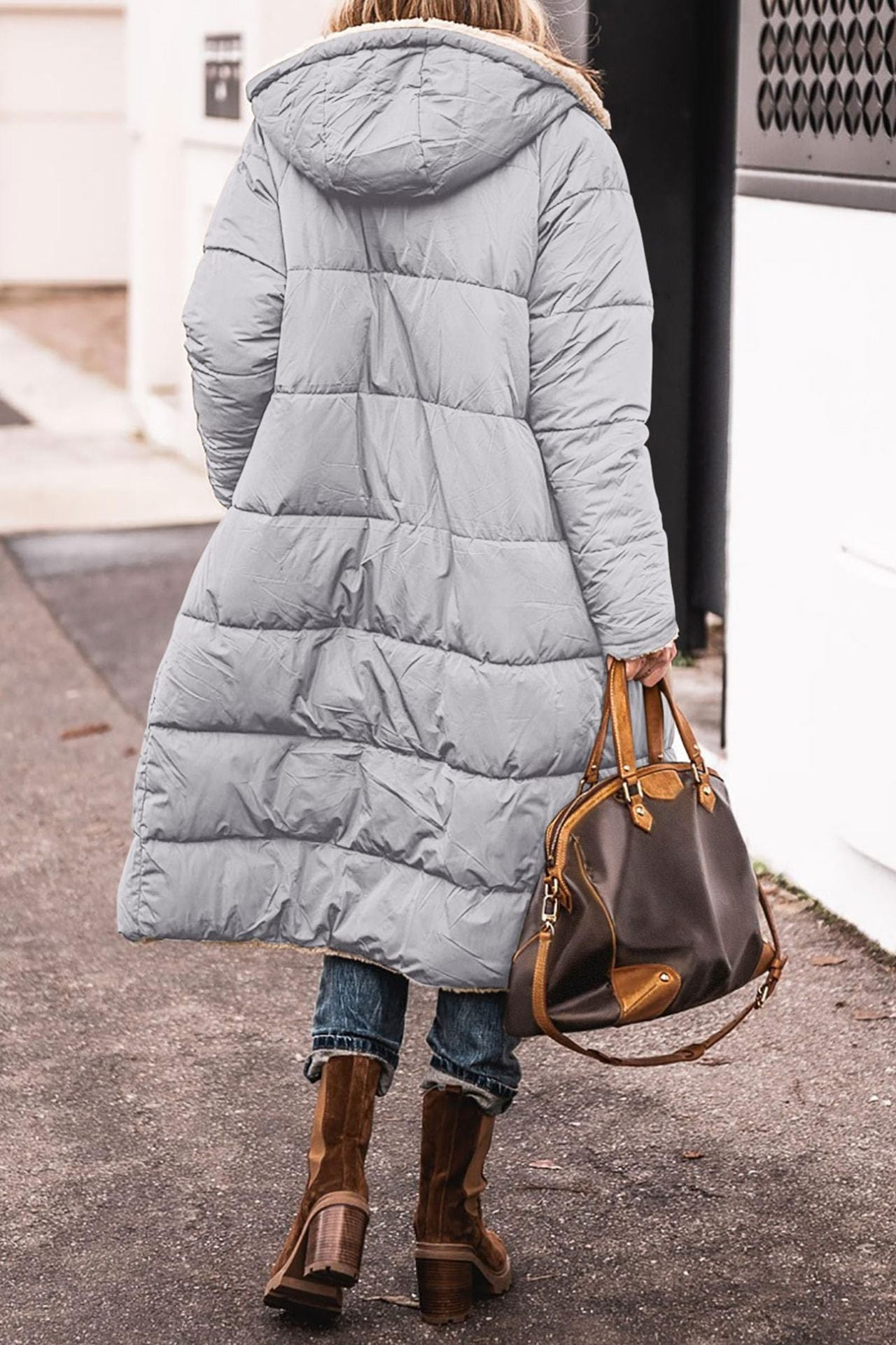 Frau in grauem Daunenmantel mit Kapuze, braune Lederstiefel, braune Handtasche, Straße.