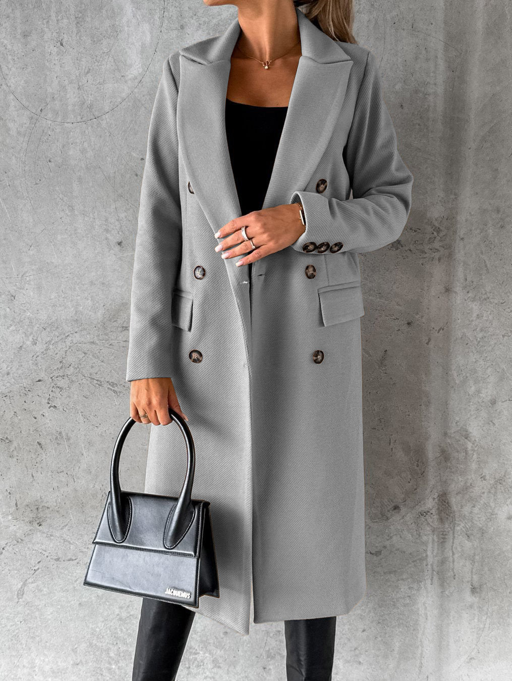 Frau in grauem Wollmantel mit Knöpfen, hält schwarze Handtasche, elegante Herbstmode.