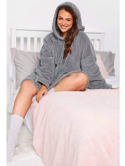 Frau in grauem Fleece-Hoodie auf Bett, gemütliche Kleidung, Wintermode, entspannter Look.