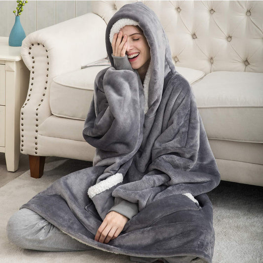 Frau in grauem, flauschigem Kapuzenpullover auf Sofa, gemütliche Winterkleidung.