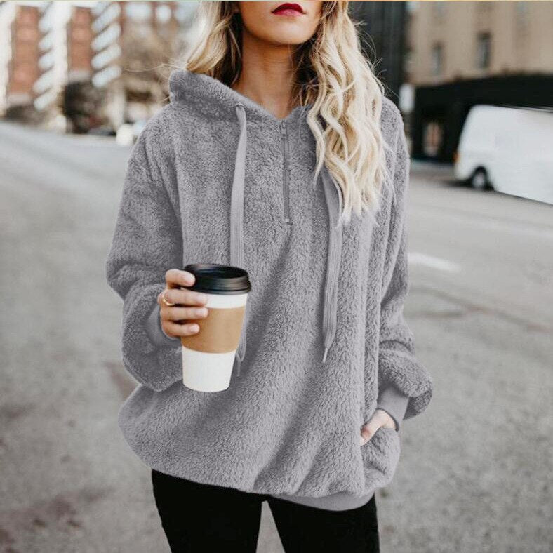 Frau in grauem Fleece-Hoodie mit Kaffeebecher, lässige Straßenmode, Herbstbekleidung.