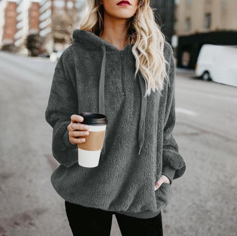 Frau in grauem Fleece-Hoodie mit Kaffeebecher, lässige Straßenmode, Herbstbekleidung.
