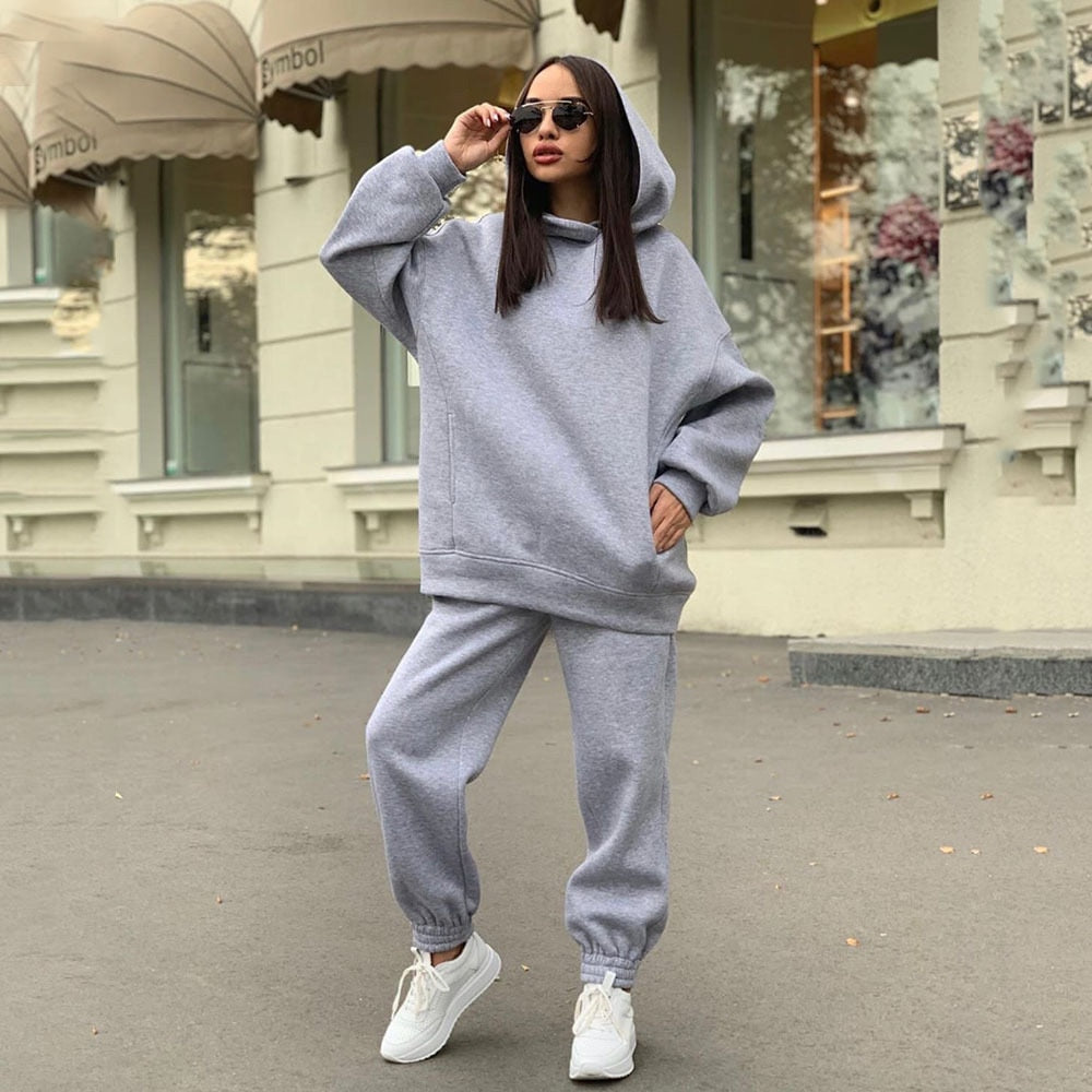 Frau in grauem Hoodie und Jogginghose, trägt Sonnenbrille, lässige Straßenmode, Herbst.
