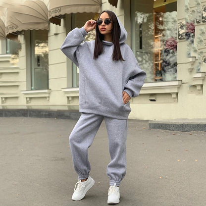 Frau in grauem Hoodie und Jogginghose, trägt Sonnenbrille, lässige Straßenmode, Herbst.