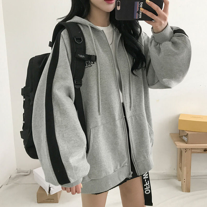 Frau in grauem Kapuzenpullover mit schwarzen Streifen, Rucksack, Smartphone, modisch, lässig.
