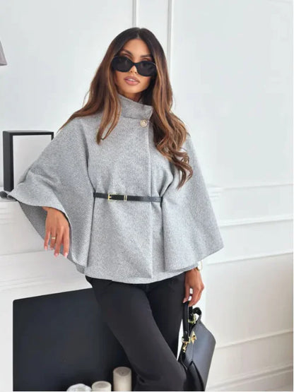 Frau in grauem Poncho mit Gürtel, schwarze Hose, Sonnenbrille, Handtasche, modisch, elegant.