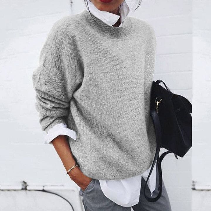 Frau in grauem Pullover, weißer Bluse, grauer Hose, schwarze Tasche, lässiger Herbstlook.