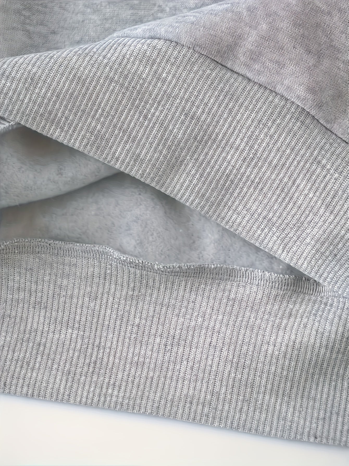 Grauer Baumwollpullover, Nahaufnahme, weiches Material, gerippter Saum, gemütliche Kleidung.