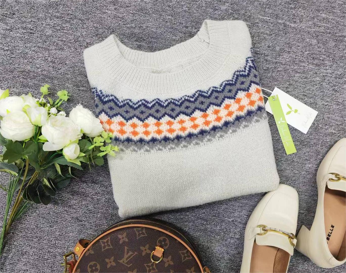 Grauer Strickpullover mit buntem Muster, weiße Blumen, braune Tasche, weiße Schuhe.