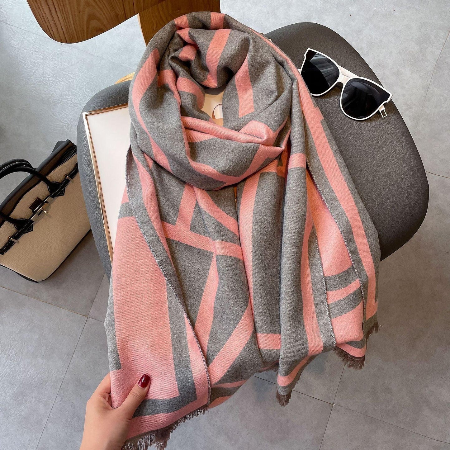 Grauer und rosa Schal mit geometrischem Muster auf Stuhl, neben Sonnenbrille und Handtasche.
