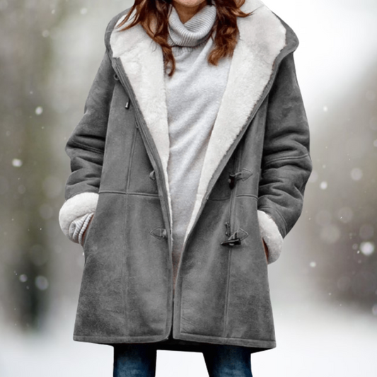 Frau in grauem Wintermantel mit Kapuze und weißem Futter im Schnee.