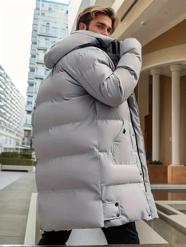 Mann in grauem Daunenmantel, Wintermode, warm, stilvoll, städtische Kulisse, Herrenbekleidung.