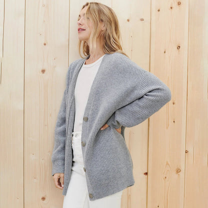 Frau trägt grauen Strickcardigan, Holz-Hintergrund, modisch, bequem, Damenmode, Herbstkleidung.