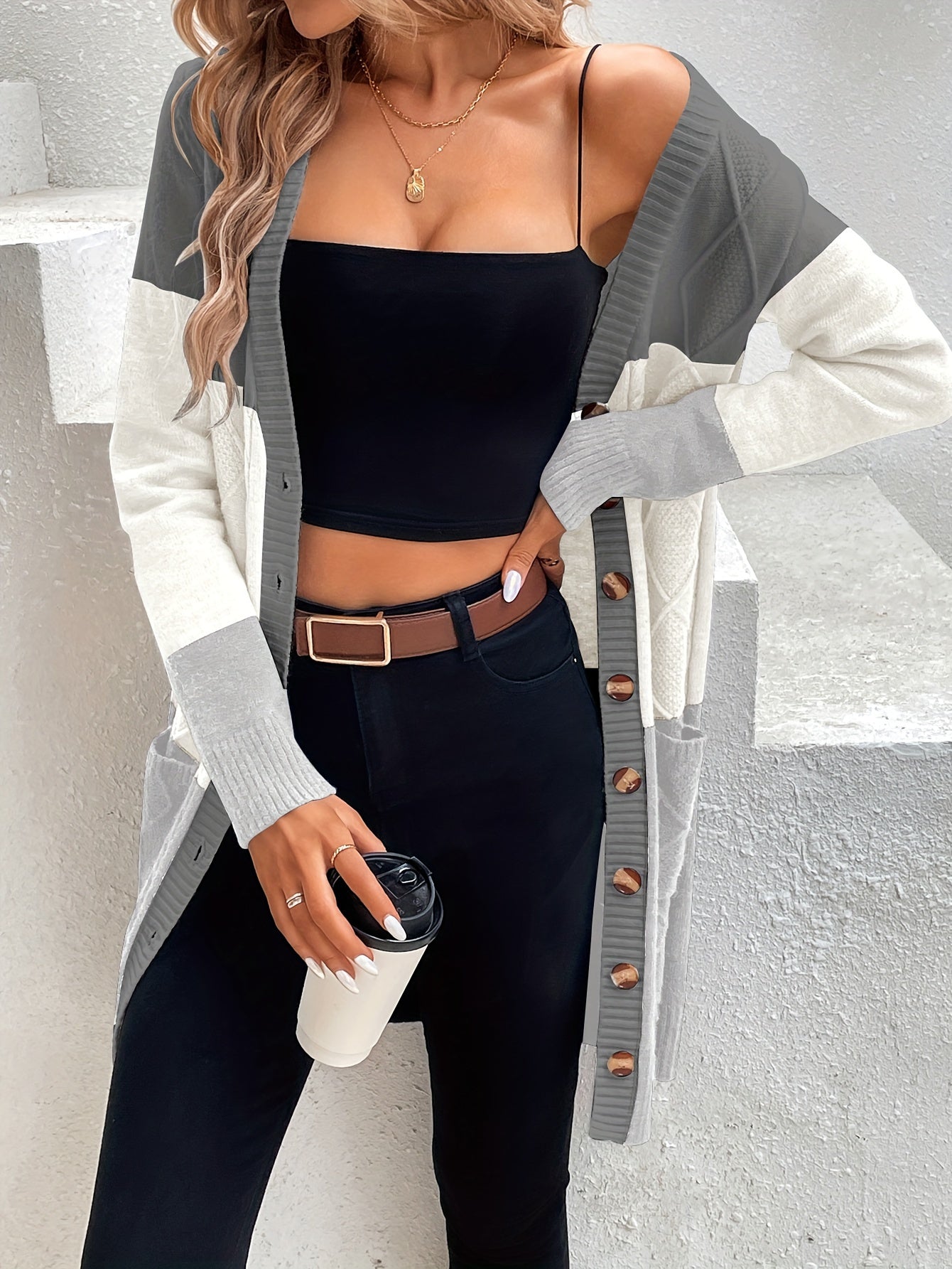 Frau in grauem Strickcardigan, schwarzem Top, Jeans, hält Kaffeebecher, modisch, lässig.