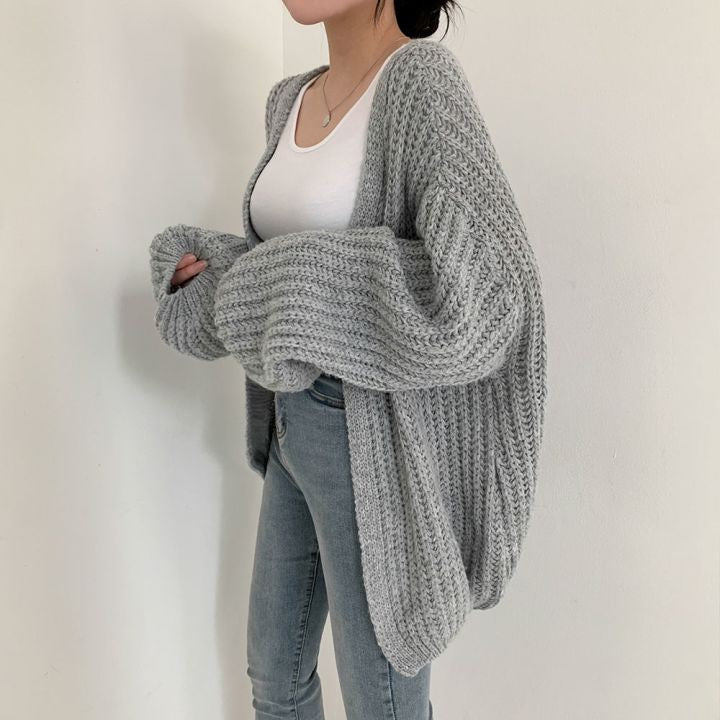 Frau trägt grauen Strick-Cardigan, weißes Top, blaue Jeans, lässige Mode, gemütlicher Look.