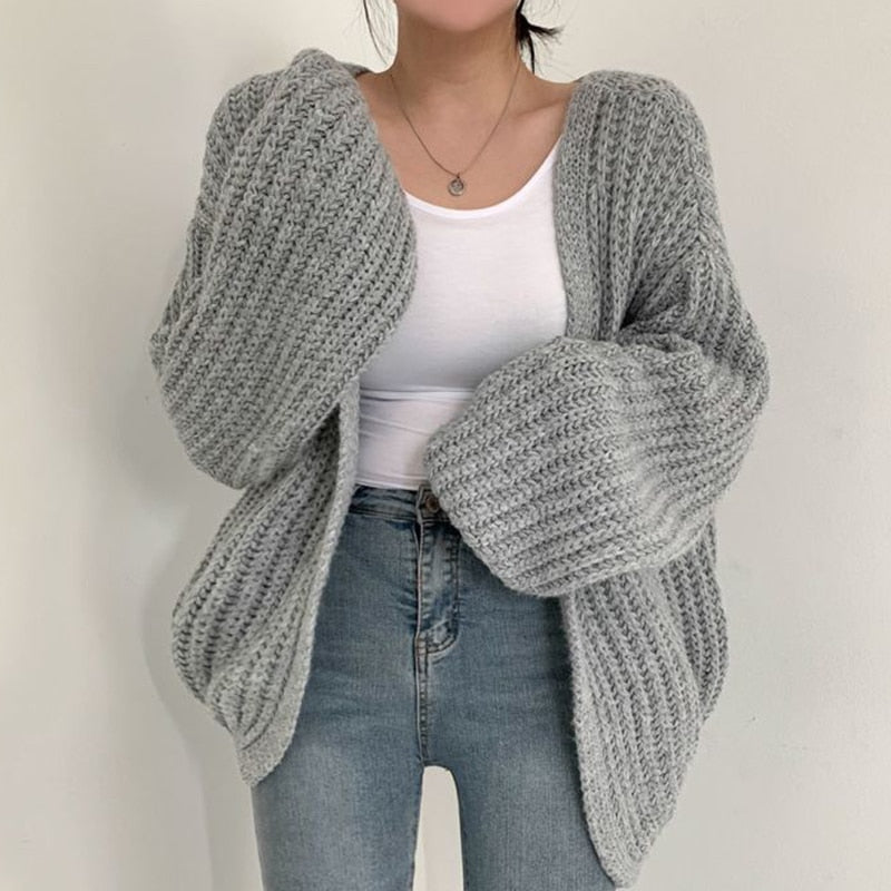 Frau trägt grauen Strick-Cardigan, weißes Top, blaue Jeans, modisch, gemütlich, Herbstmode.