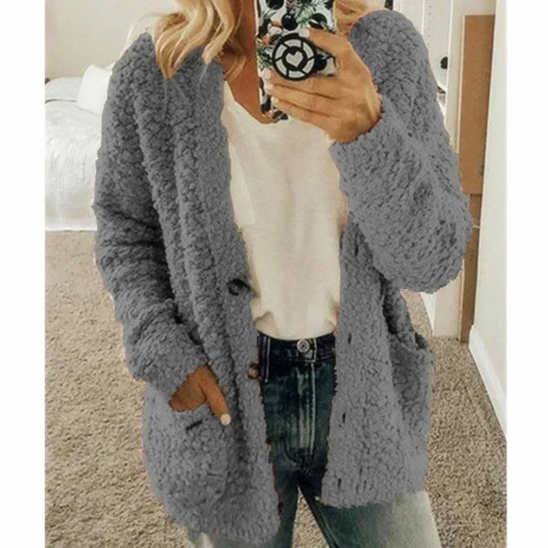 Frau in grauer Strickjacke, weißem T-Shirt und Jeans, hält Smartphone, gemütliche Herbstmode.