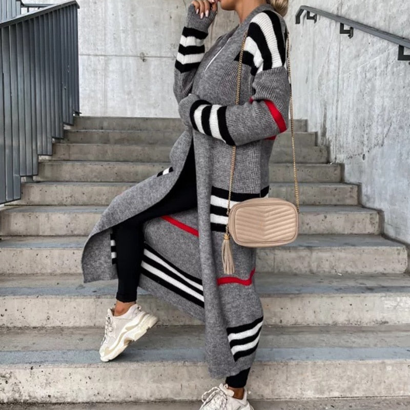Frau in grauem Strickmantel mit Streifen, beige Umhängetasche, weiße Sneaker, Treppe.