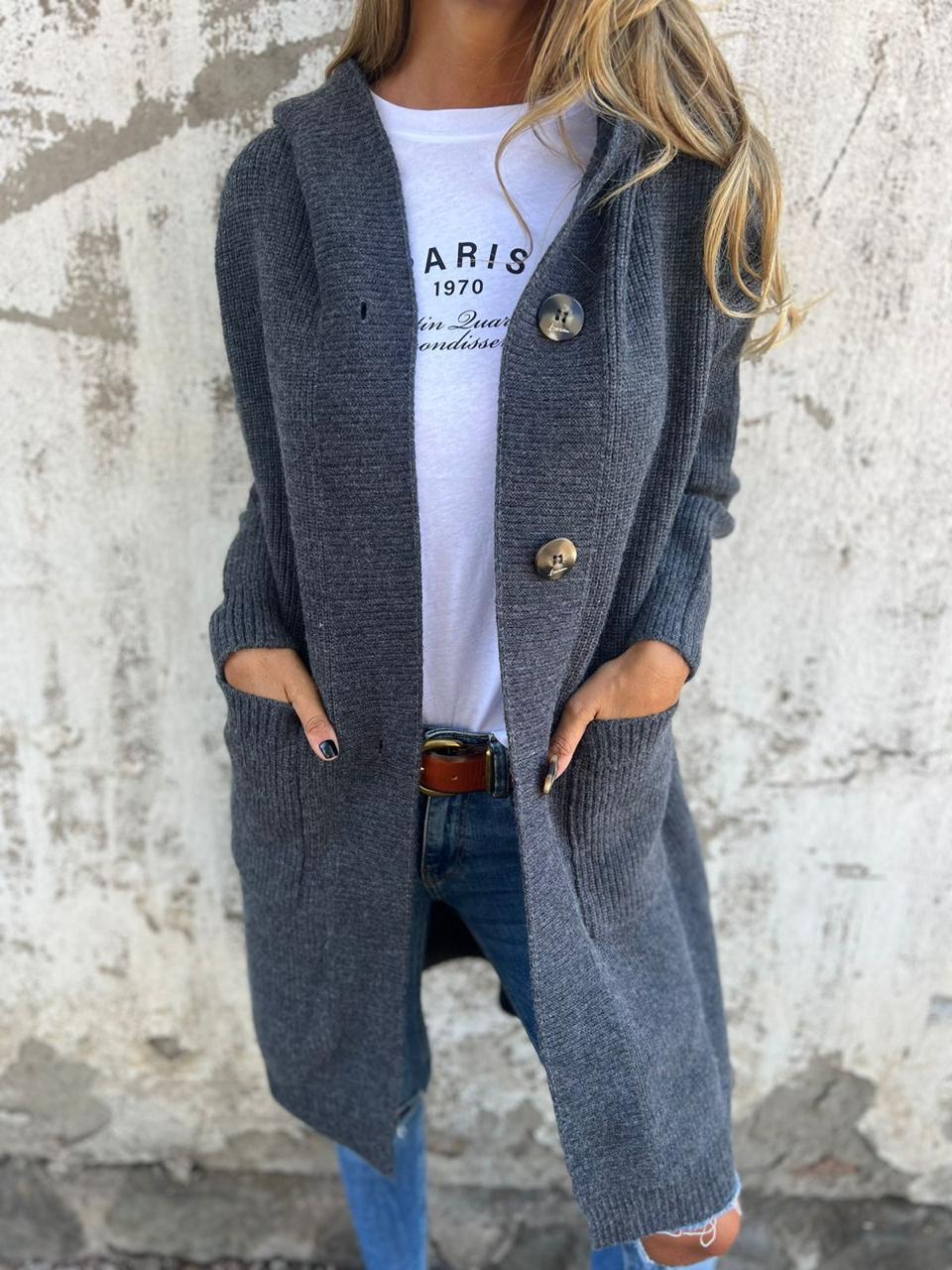 Frau in grauem Strickmantel mit Kapuze, weiße Paris-T-Shirt, blaue Jeans, lässiger Herbstlook.