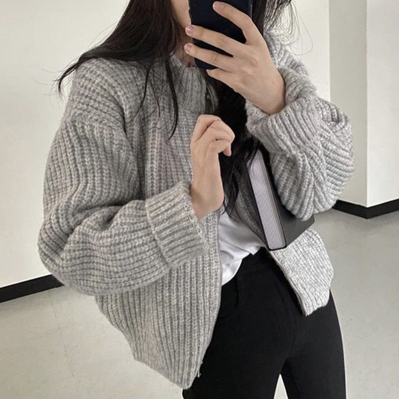 Frau in grauem Strickpullover, hält Smartphone, modisch, gemütlich, Herbstmode, Innenraum.