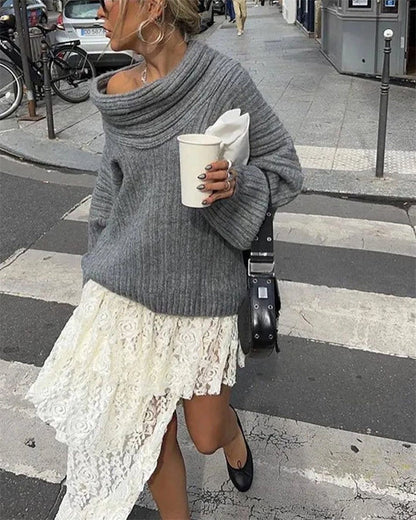 Frau in grauem Strickpullover und weißem Spitzenrock, hält Kaffeebecher, modisch, urban.