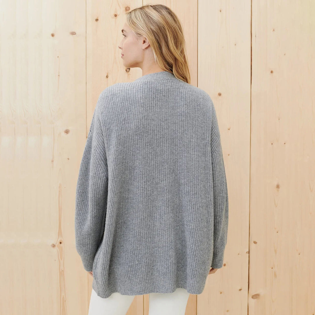Frau in grauem Strickpullover aus Wolle, Rückansicht, vor Holzwand.