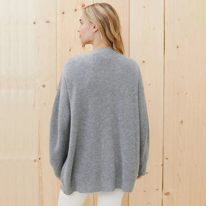 Frau in grauem Strickpullover, Rückansicht, vor Holzwand, lässige Mode, Herbstbekleidung.