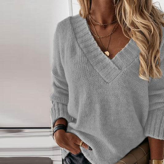 Frau in grauem Strickpullover mit V-Ausschnitt, modische Ketten, blonde Haare, lässiger Stil.